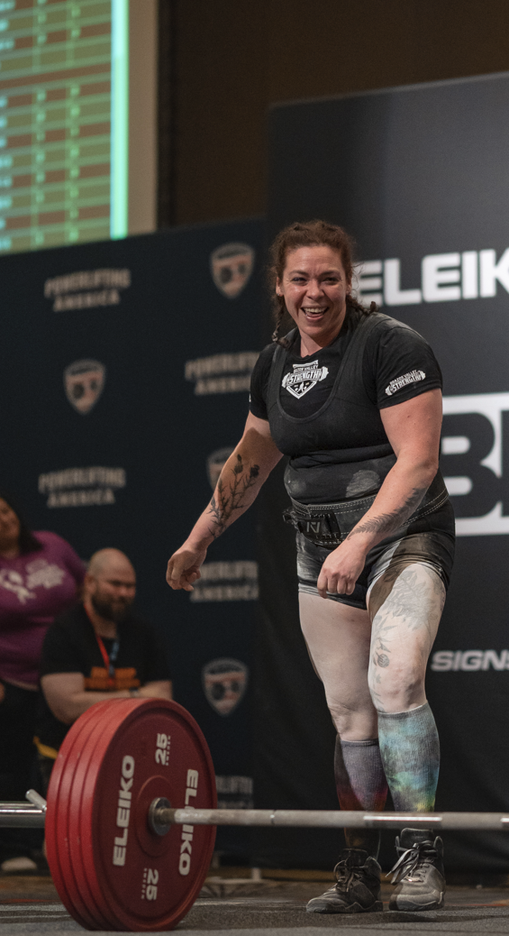 Woman lifting weights at a weightlifting competition with 'Eleiko' branding in the background.