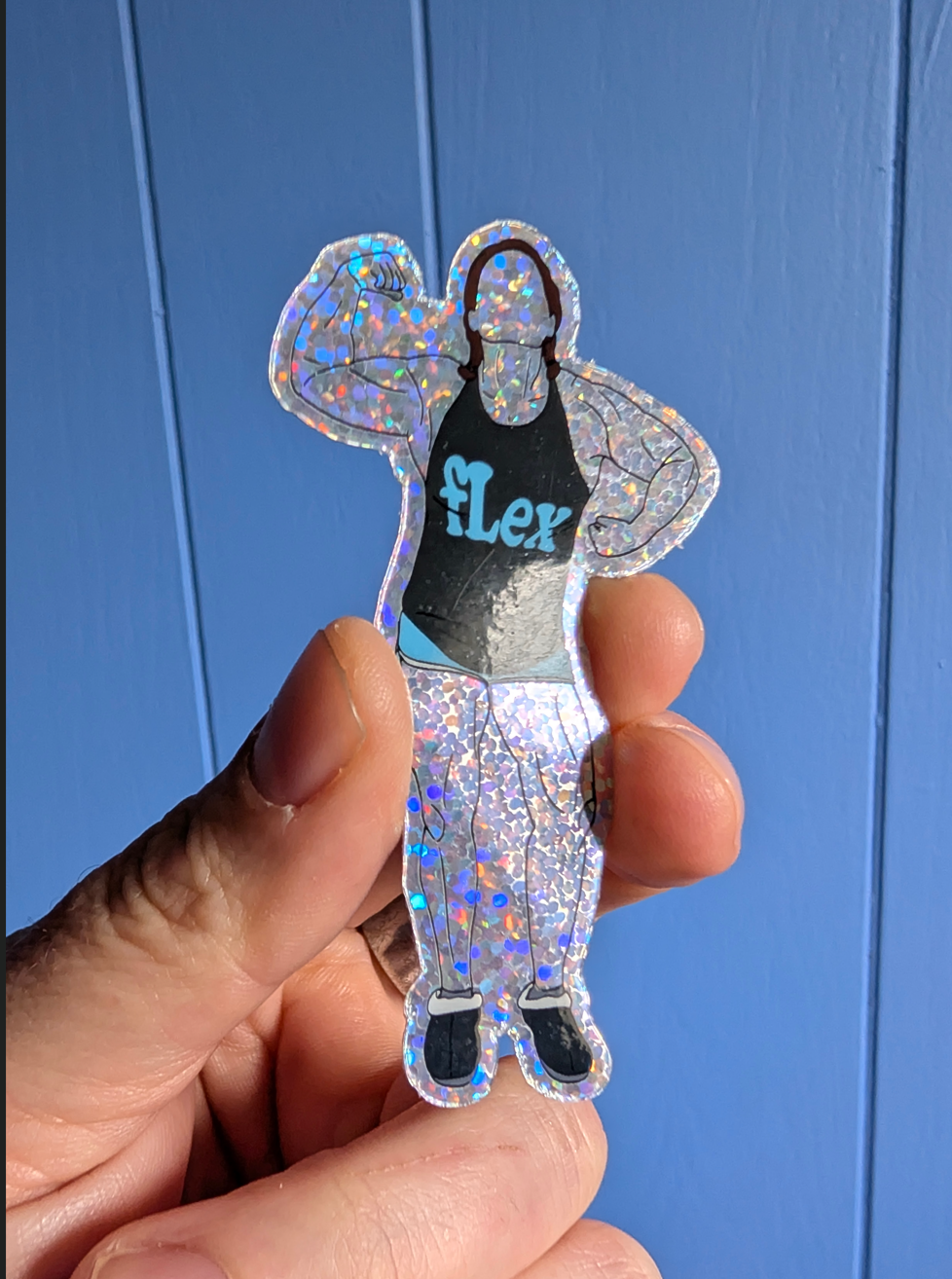 Hand holding a glittery 'Flex' sticker against a blue background