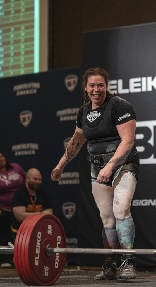 Woman lifting weights at a weightlifting competition with 'Eleiko' branding in the background.